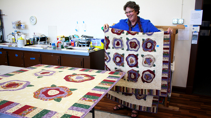 Woman holding quilt looking at painting of a quilt block on table